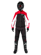 Motorcrosser in Alpinestars Lite-Dura Softshell Jas in zwart, felrood en wit, gecombineerd met een zwarte off-road broek, zwart-witte laarzen en een zwarte helm met crossbril, complete uitrusting voor enduro racing