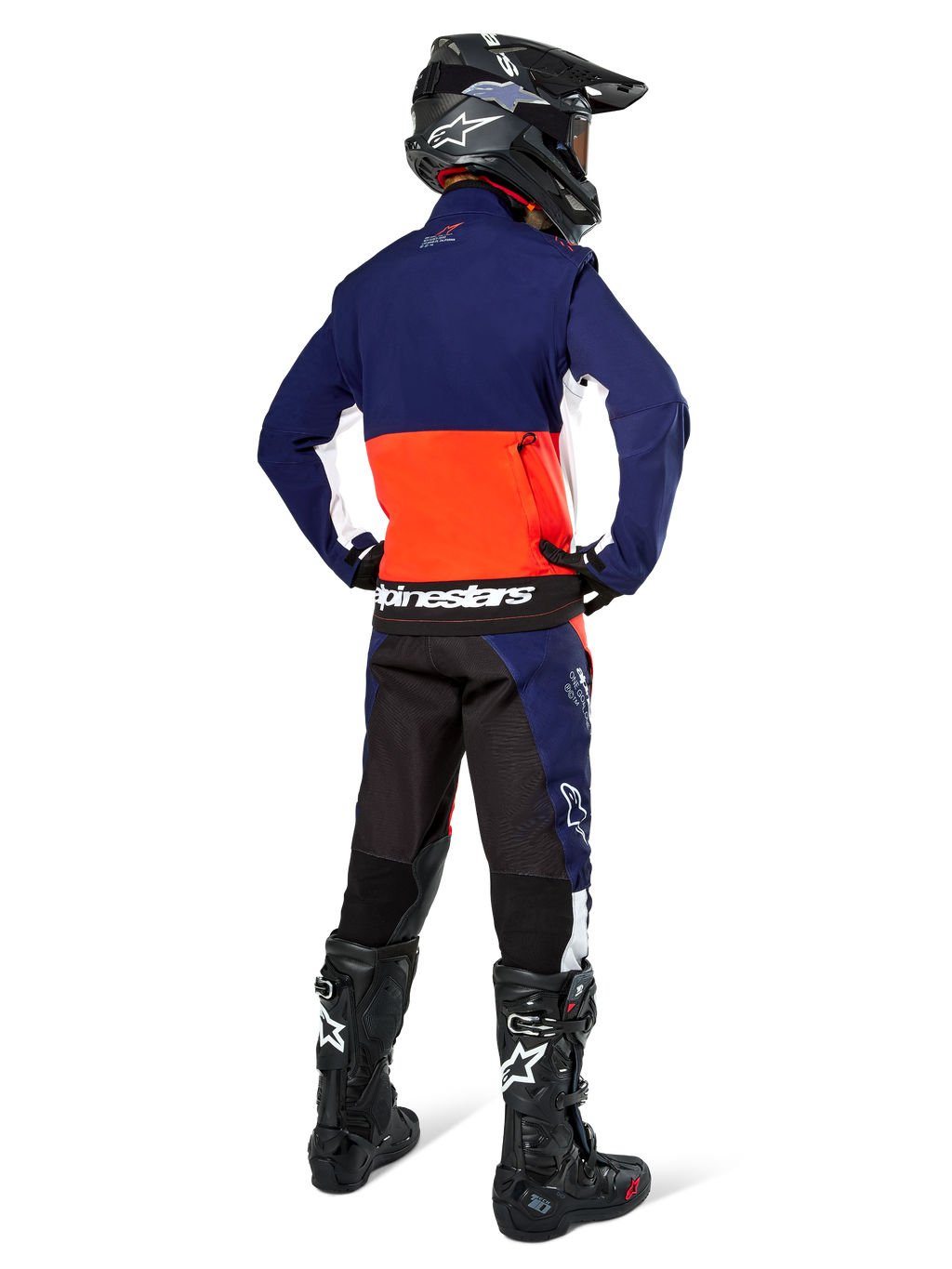 Motorcrosser vanaf de achterkant in Alpinestars Lite-Dura Softshell Jas in navy, feloranje en wit, met grote opbergzak op de rug, gecombineerd met bijpassende endurobroek, zwarte motorcrosshelm en zwarte off-road laarzen