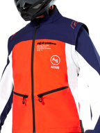 Alpinestars Lite-Dura Softshell Jas, navy, hot orange en wit, close-up van de torso, met een feloranje voorpand, witte zijpanelen en marineblauwe schouders, handzakken met rits en opvallende Alpinestars-branding, gedragen door een rijder met een zwarte off-road helm