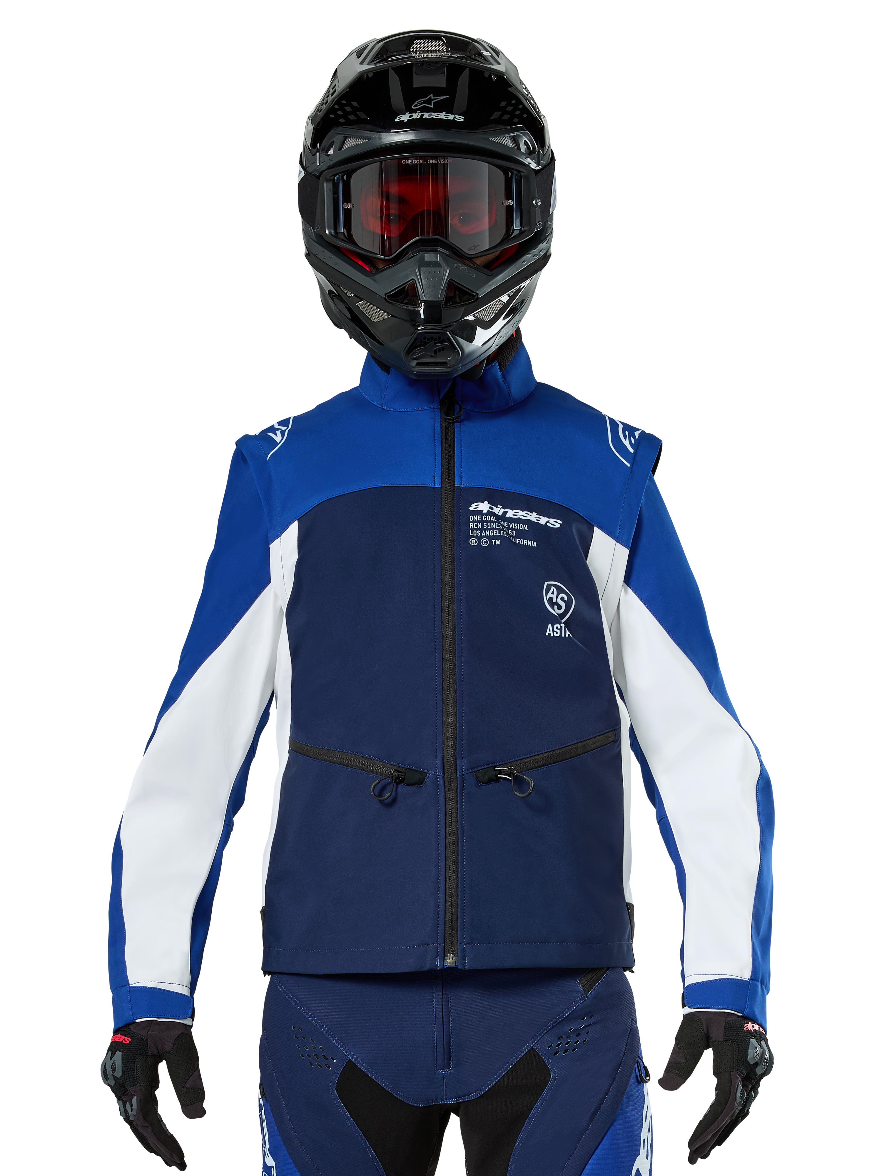 Motocross-rijder met de Alpinestars Lite-Dura Softshell Jas in Navy Bright Blue White, vooraanzicht, gecombineerd met een zwarte helm en een bril met rode glazen, voorzien van een technisch winddicht ontwerp met ritszakken en witte accenten voor off-road enduro rijden