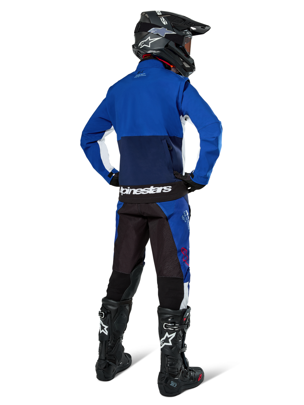 Motocrossrijder van achteren gezien die de Alpinestars Lite-Dura Softshell Jas in Navy Bright Blue en wit draagt, gecombineerd met bijpassende endurobroek, zwarte helm en zwarte laarzen, complete off-road race-uitrusting