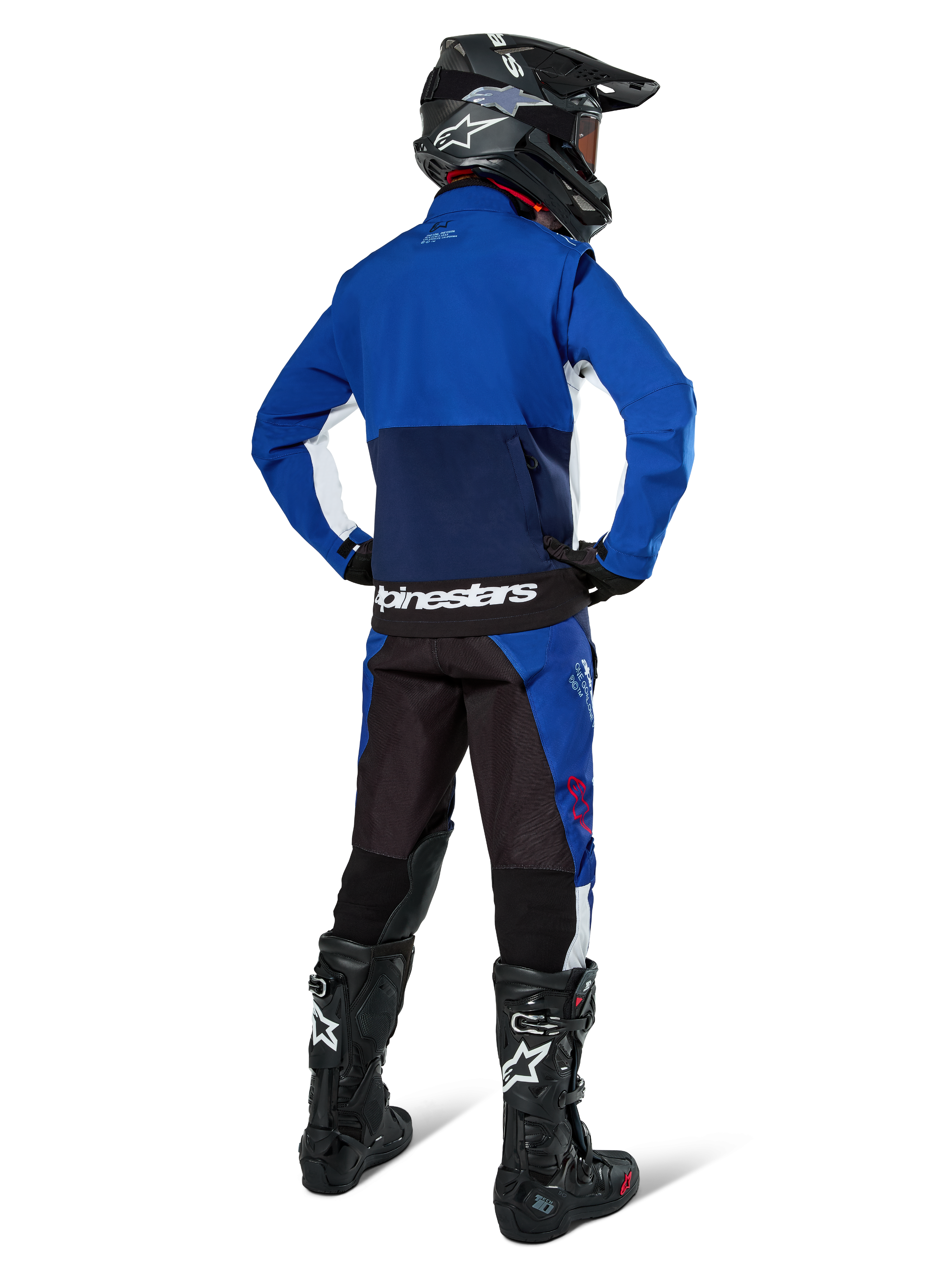 Motocrossrijder van achteren gezien die de Alpinestars Lite-Dura Softshell Jas in Navy Bright Blue en wit draagt, gecombineerd met bijpassende endurobroek, zwarte helm en zwarte laarzen, complete off-road race-uitrusting