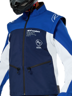 Alpinestars Lite-Dura Softshell Jas, motorcross- en endurojas, marineblauw, helderblauw en wit, met witte Alpinestars-branding op de borst en zakken met rits, gedragen met een zwarte helm, duurzame softshell-constructie met afneembare mouwen voor off-road rijden