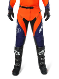 Alpinestars Pro-Dura Pants, motorcross- en endurobroek, marineblauw, feloranje en wit, met zwarte panelen en witte logo's, gedragen met zwarte off-road laarzen en handschoenen, professionele beschermende uitrusting voor trail- en off-road rijden