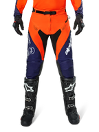 Alpinestars Pro-Dura Pants, motorcross- en endurobroek, marineblauw, feloranje en wit, met zwarte panelen en witte logo's, gedragen met zwarte off-road laarzen en handschoenen, professionele beschermende uitrusting voor trail- en off-road rijden