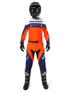 Motocrossrijder in Alpinestars Pro-Dura broek in Navy Hot Orange White, met bijpassende jersey met lange mouwen, zwarte helm met crossbril, zwarte handschoenen en zwarte motorcrosslaarzen, complete off-road race-uitrusting.