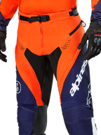 Alpinestars Pro-Dura broek, enduro motorbroek, marineblauw, feloranje en wit, detailweergave van de taille met SX2 magnetische gesp en ventilatieopeningen met rits op de dijen, duurzaam ripstop-materiaal met opvallende branding, gedragen met bijpassende uitrusting