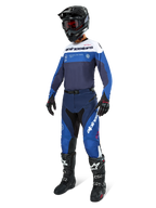 Motocross-rijder in Alpinestars Pro-Dura broek in marineblauw, felblauw en wit, gecombineerd met een bijpassende jersey met lange mouwen, zwarte helm met rode bril, zwarte handschoenen en zwart-witte laarzen, gecoördineerde outfit voor enduro en off-road racing.