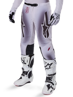 Alpinestars 2025 Supertech Maker crossbroek, motorcross broek, zilver en zwart, met grote sterlogo's en rode belettering, getoond met bijpassende witte laarzen en handschoenen