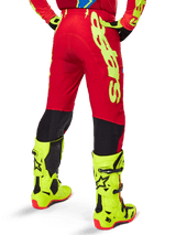 Alpinestars 2025 Supertech Maker broek, motorcrossbroek, helderrood en fluogeel, achteraanzicht met grote gele branding aan de zijkant en zwarte panelen op de onderbenen, gedragen met bijpassende fluogele laarzen en uitrusting