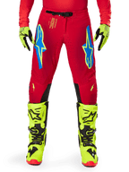 Alpinestars 2025 Supertech Maker broek, motorcrossbroek, felrood en fluogeel, met blauwe Astars-logo's op de dijen, geventileerde perforaties en zwarte panelen aan de binnenzijde van de knie, gedragen met bijpassende fluogele laarzen en handschoenen