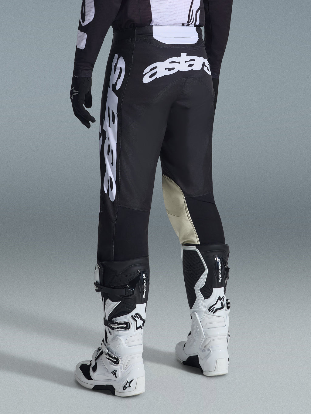 Rear view of Alpinestars 2026 Racer Air Riway Pants in Black and White, featuring prominent white 'astars' branding on the seat and leg, cream leather inner knee panels, worn with matching black and white motocross boots and jersey.