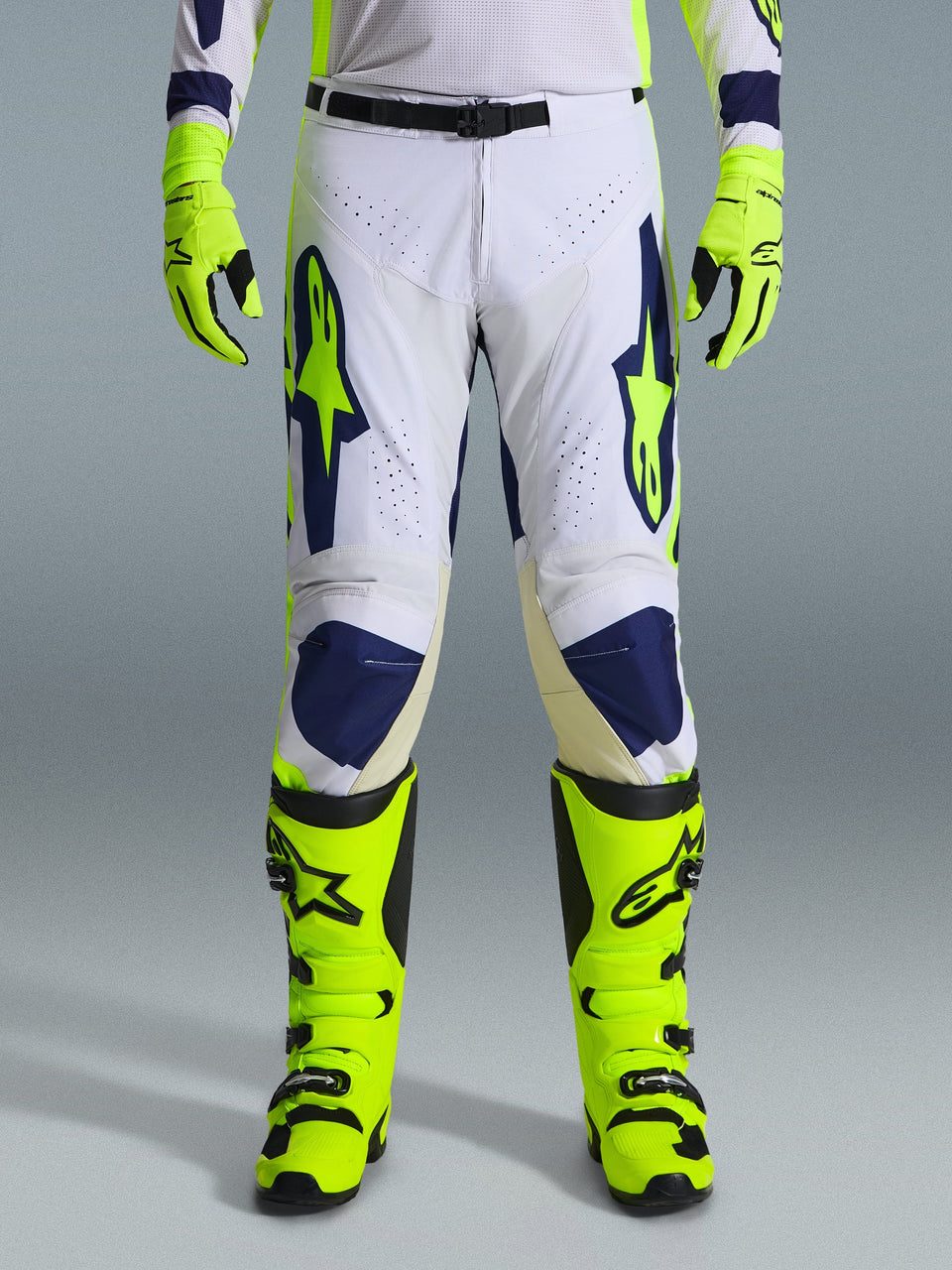Alpinestars 2026 Racer Air Riway broek, motorcrossbroek, lichtgrijs, fluogeel en blauw, gedragen met bijpassende neongele handschoenen en laarzen, voorzien van geperforeerde voorpanelen voor luchtstroom en opvallende blauwe en gele branding, sportief ontwerp voor off-road prestaties