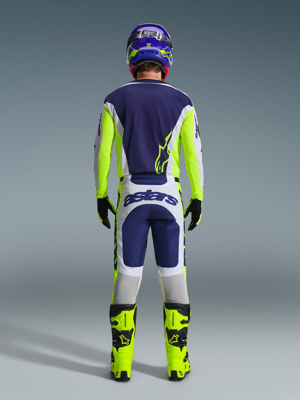 Motocross rider from the back wearing the Alpinestars 2026 Racer Air Riway Pants in Light Gray, Yellow Fluo, and Blue, paired with a matching jersey and bright yellow boots, illustrating a complete professional off-road racing gear set.