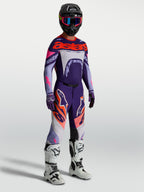 Alpinestars Supertech Dyna broek, heren motocrossbroek, paars en roze fluo, gedragen met bijpassende jersey en witte laarzen.
