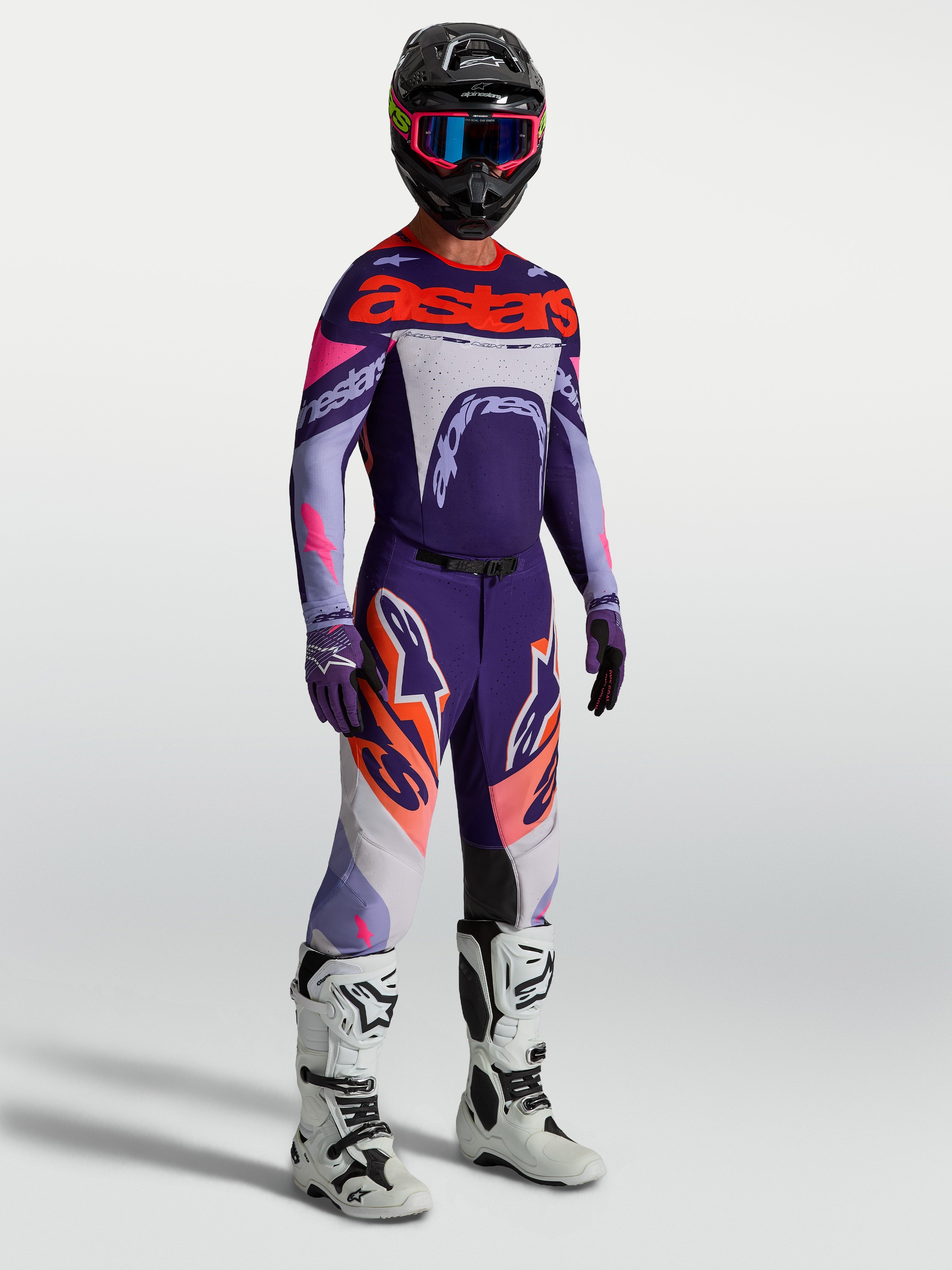 Alpinestars Supertech Dyna broek, heren motocrossbroek, paars en roze fluo, gedragen met bijpassende jersey en witte laarzen.