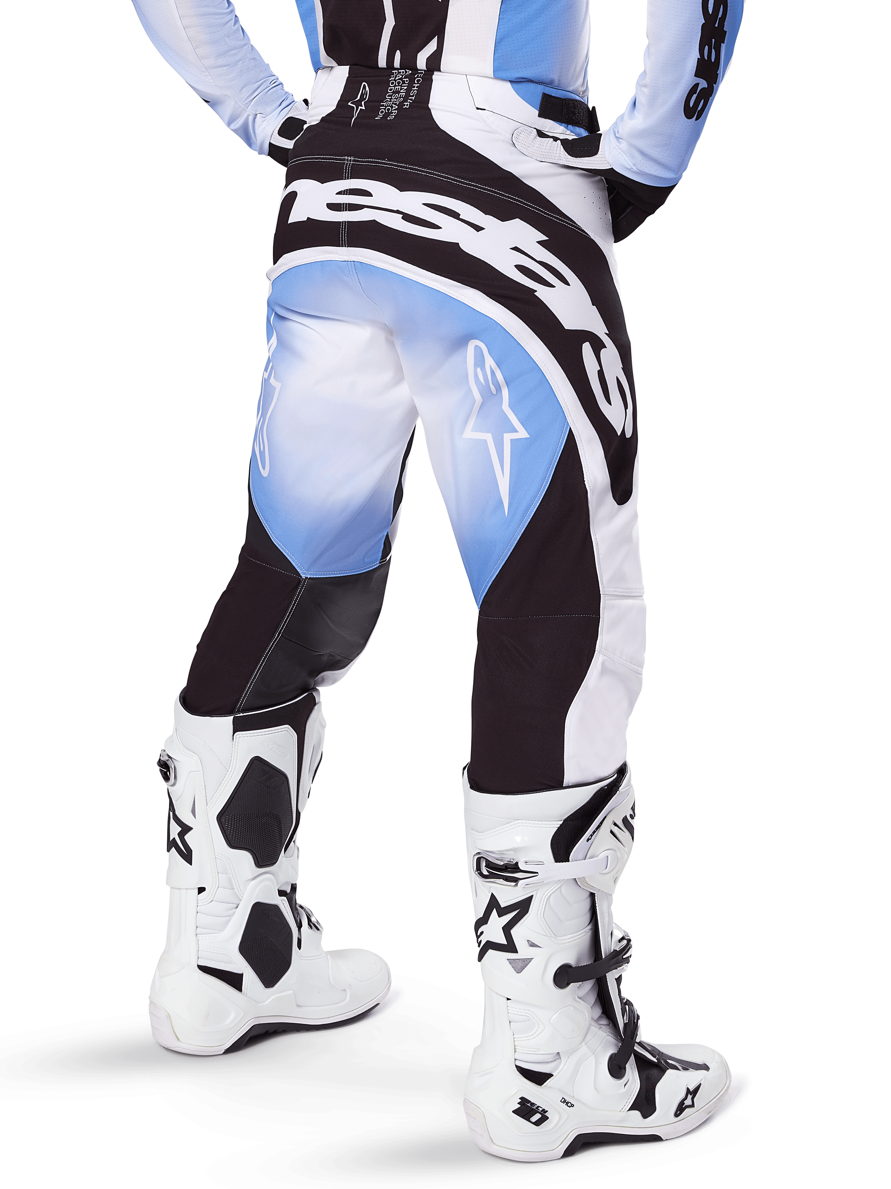 Alpinestars 2025 Techstar Melt crossbroek, motorcrossbroek, zwart, blauw en wit, achteraanzicht met opvallend Alpinestars-woordmerk op het zitvlak en sterlogo's op de pijpen, gedragen met witte en zwarte Tech 10-laarzen, professionele off-road race-uitrusting