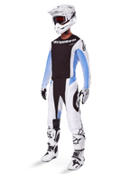 Motorcrossrijder in de Alpinestars 2025 Techstar Melt broek, wit-zwarte motorcrosskleding met lichtblauwe accenten, bijpassende jersey en handschoenen, witte helm en crossbril, witte en zwarte racelaarzen, professionele off-road uitrusting.