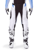 Alpinestars 2025 Techstar Melt broek, motorcross broek, wit en zwart met lichtblauwe accenten, gedragen met bijpassende witte en zwarte laarzen en handschoenen, voorzien van lasergesneden perforaties en hoogwaardig race-ontwerp.