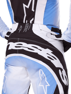 Alpinestars 2025 Techstar Melt broek, motocrossbroek, zwart, wit en blauw, close-up achteraanzicht met opvallende witte branding op het zitvlak, gecombineerd met bijpassende Techstar Melt jersey en handschoenen, professionele race-uitrusting voor motocross