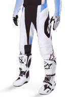 Alpinestars 2025 Techstar Melt crossbroek, motorcross broek, wit en zwart met blauwe accenten, met laser-gesneden perforaties voor luchtstroom en Babel-knieconstructie, gedragen met bijpassende witte motorcrosslaarzen en handschoenen, atletisch off-road race-ontwerp