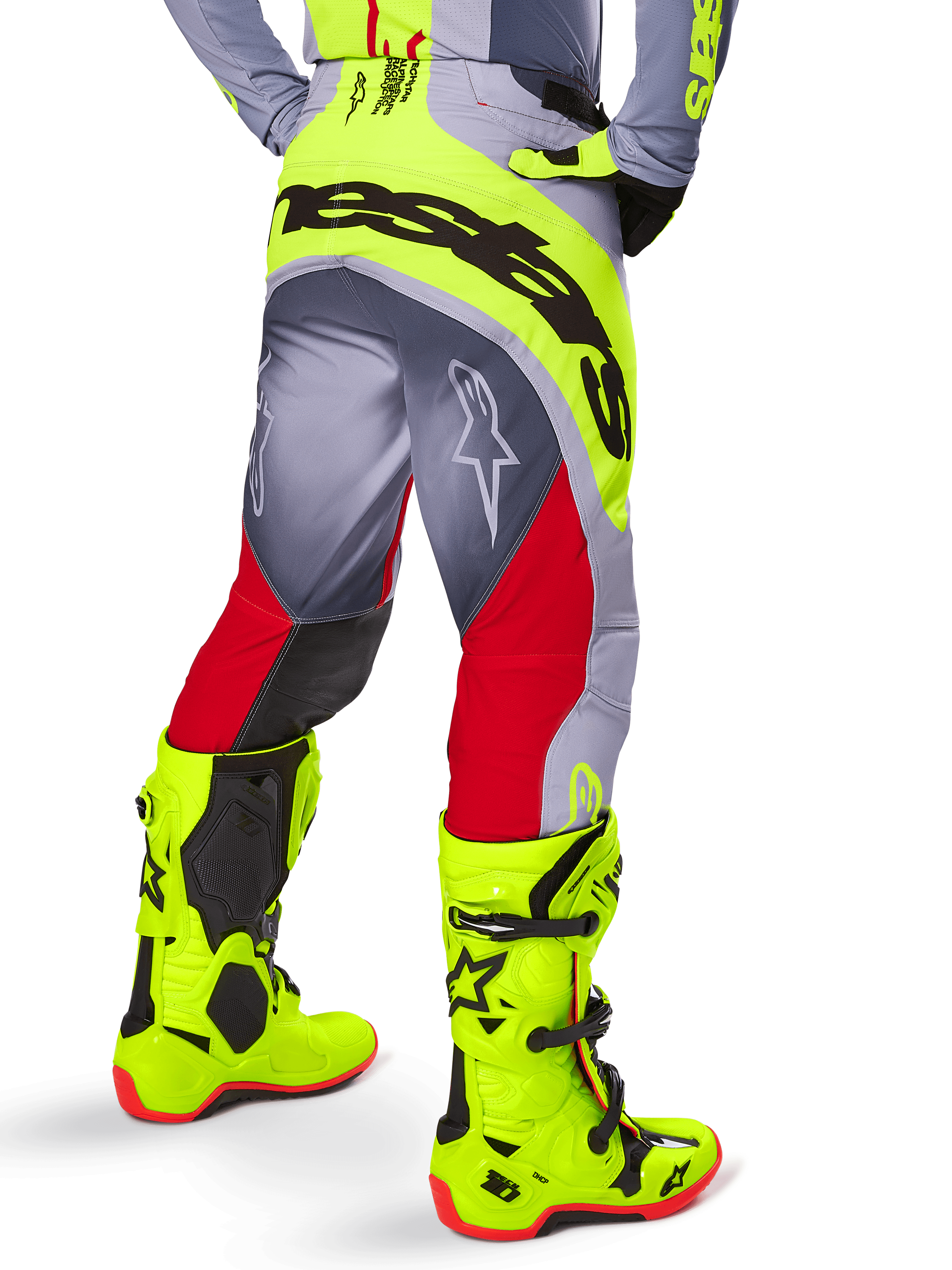 Alpinestars 2025 Techstar Melt crossbroek, motorcross broek, helderrood en grijs met neongele accenten, achteraanzicht met grote zwarte branding op het zitvlak, gedragen met bijpassende felgele laarzen en een grijs shirt, atletische racepasvorm voor off-road competitie.