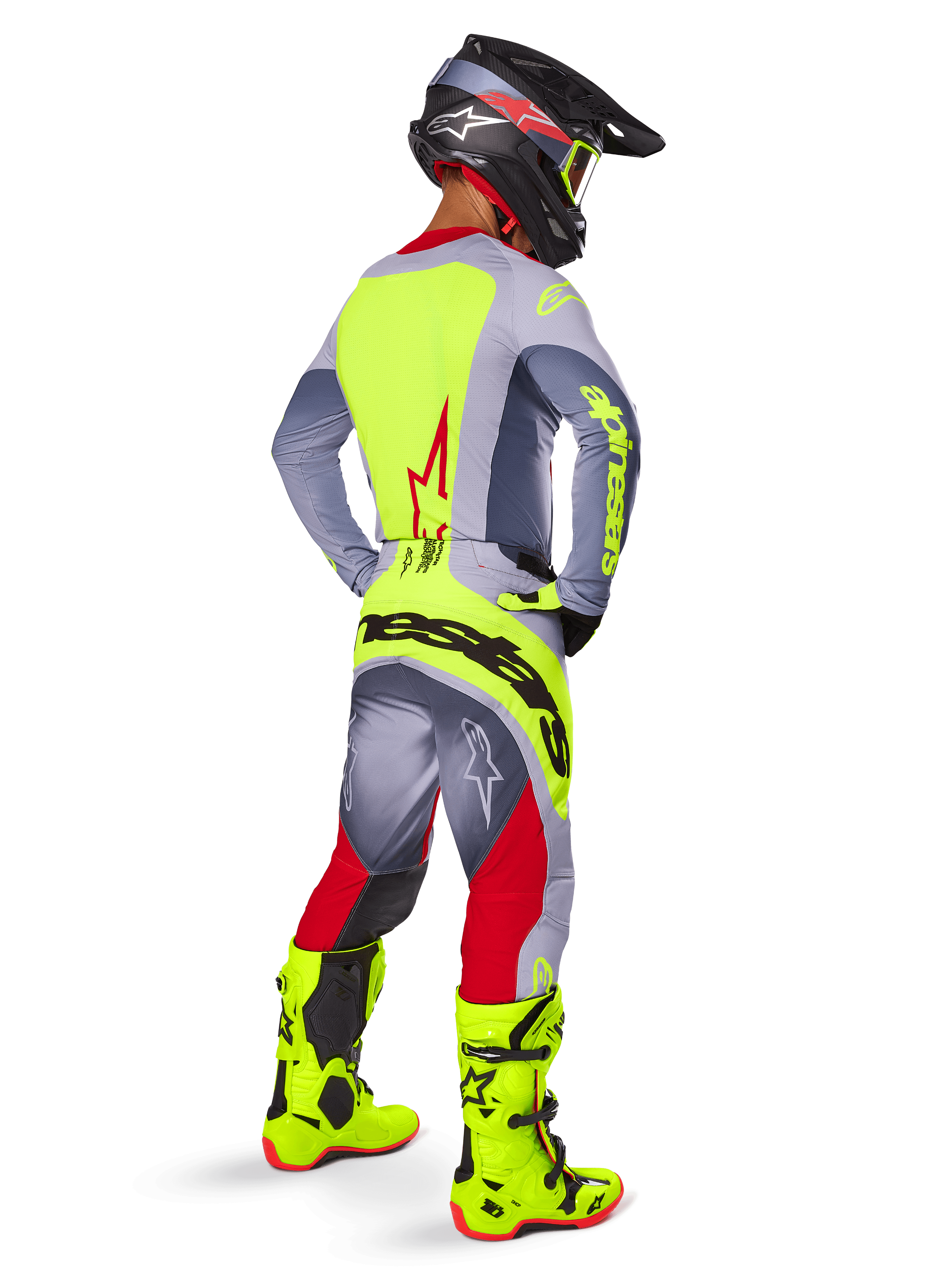 Motorcrosser in drie-kwart achteraanzicht, draagt Alpinestars 2025 Techstar Melt broek in felrood en grijs, met een opvallend neongeel logo op het zitvlak, bijpassende grijze en neongele jersey, felgekleurde neongele laarzen en een zwarte helm met neon crossbril, professionele off-road race-uitrusting.