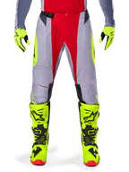 Alpinestars 2025 Techstar Melt crossbroek, motocrossbroek, helderrood en grijs met fluorescerend gele accenten, gedragen met bijpassende neongele handschoenen en laarzen, voorzien van een magnetische taillegesp en lasergesneden perforaties voor ventilatie.