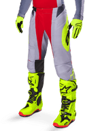 Alpinestars 2025 Techstar Melt broek, motorcross broek, helderrood en grijs met een opvallend neongeel logo, gedragen met bijpassende neongele handschoenen en laarzen, atletische pasvorm voor motorcrossraces