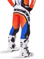 Alpinestars 2025 Techstar Melt broek, motorcross broek, oranje en blauw, van achteren gezien, met groot wit logo op het zitvlak, gedragen met bijpassend oranje shirt en witte Tech 10 laarzen, duurzame off-road race-uitrusting