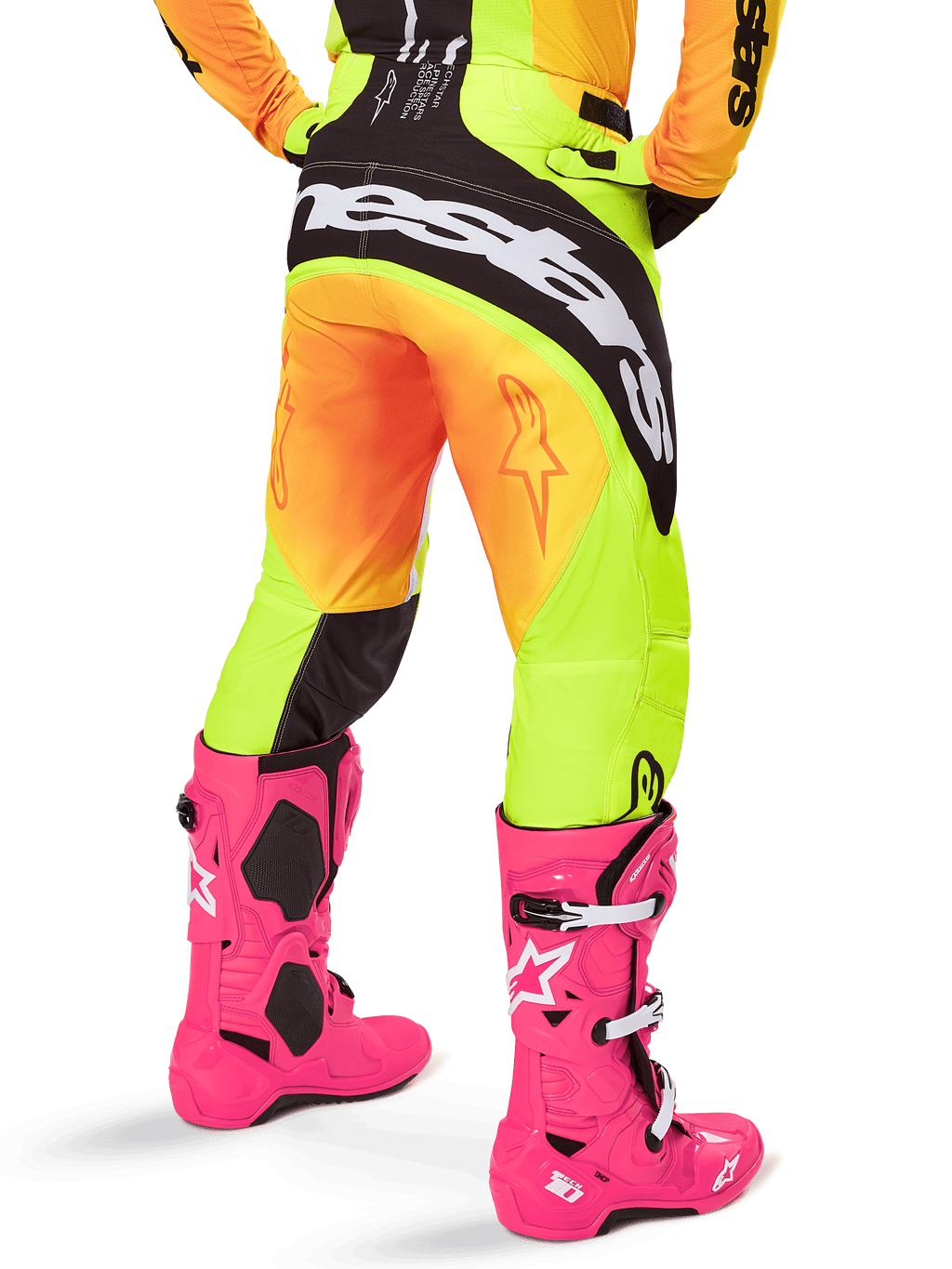 Achteraanzicht van een motorcrosser met Alpinestars 2025 Techstar Melt broek, geel en oranje kleurverloop met zwart-witte branding op het zitvlak, gecombineerd met felroze motorcrosslaarzen, performance off-road uitrusting.