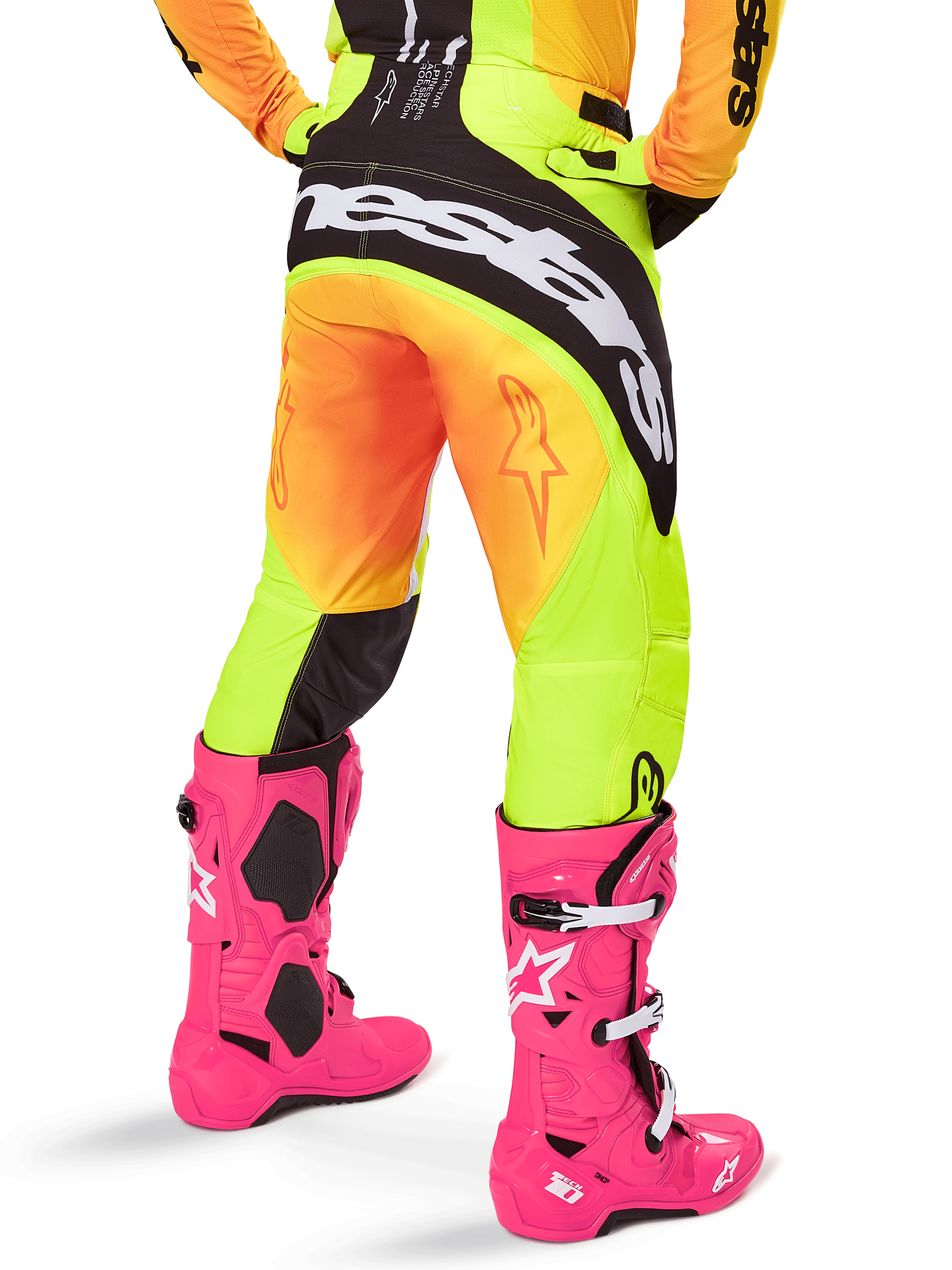 Achteraanzicht van een motorcrosser met Alpinestars 2025 Techstar Melt broek, geel en oranje kleurverloop met zwart-witte branding op het zitvlak, gecombineerd met felroze motorcrosslaarzen, performance off-road uitrusting.
