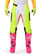 Alpinestars 2025 Techstar Melt crossbroek, motorcross broek, neongeel en wit met oranje accenten, gedragen met bijpassende gele handschoenen en felroze motorcrosslaarzen, voorzien van geperforeerde ventilatiepanelen en een magnetische taillegesp, hoogwaardige race-uitrusting