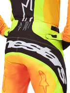 Alpinestars 2025 Techstar Melt crossbroek, motorcross broek, close-up van de achterkant, neongeel en oranje met zwarte panelen, groot wit Alpinestars-logo over het zitvlak, technische off-road motorkleding