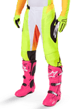 Alpinestars 2025 Techstar Melt crossbroek, motorcross broek, neongeel met witte en oranje accenten, zwarte zijpatronen, gedragen met felroze motorcrosslaarzen en neongele handschoenen, voorzien van geperforeerde ventilatie, duurzame off-road racekleding