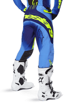 Alpinestars 2025 Techstar Melt crossbroek, motorcrossbroek, geel fluo blauw, achteraanzicht met groot geel logo op het zitvlak en donkerblauwe accenten, gedragen met witte Alpinestars Tech 10 laarzen en een bijpassende jersey.