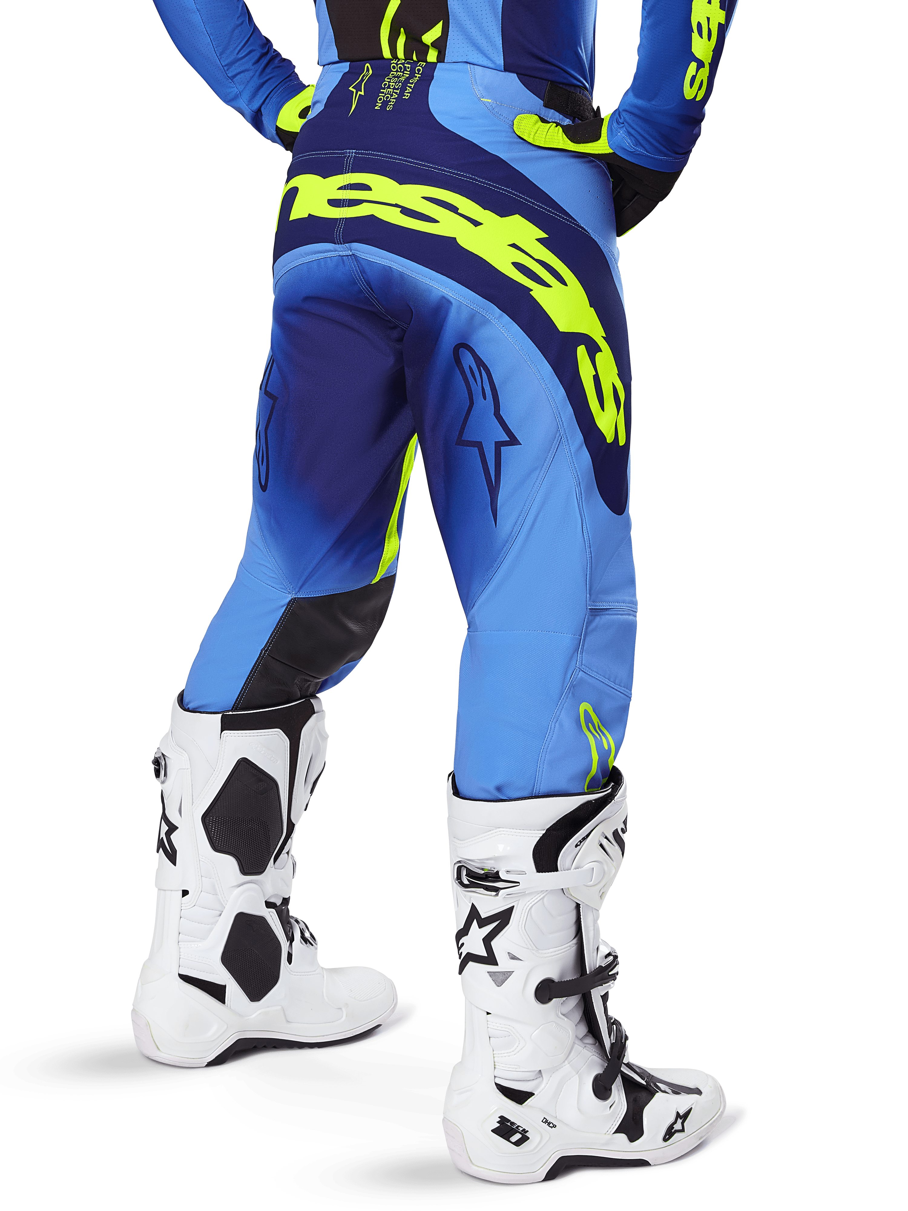 Alpinestars 2025 Techstar Melt crossbroek, motorcrossbroek, geel fluo blauw, achteraanzicht met groot geel logo op het zitvlak en donkerblauwe accenten, gedragen met witte Alpinestars Tech 10 laarzen en een bijpassende jersey.