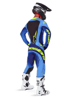 Alpinestars 2025 Techstar Melt crossbroek, motorcross kleding, Yellow Fluo Blue, achteraanzicht van een rijder met bijpassende blauwe jersey met opvallende gele branding, witte en zwarte laarzen en zwarte helm, complete race-outfit voor off-road prestaties