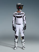 Alpinestars 2026 Racer Riway Broek, motorcrossbroek in wit en zwart, gedragen door een motocrosser met bijpassend wit shirt, zwarte helm met rode bril, zwarte handschoenen en witte laarzen, voorzien van opvallende zwarte Astars-branding, prestatiegericht ontwerp voor off-road gebruik