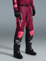 Alpinestars 2026 Racer Riway crossbroek, motorcrossbroek, Dark Red Coral, met grote roze sterlogo's en zwarte binnenpanelen op de knieën, gedragen met zwarte motorcrosslaarzen en zwarte handschoenen, atletische racepasvorm voor off-road rijden.