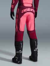 Alpinestars 2026 Racer Riway crossbroek, motorcross broek, donkerrood en koraalrood, achteraanzicht met groot koraalrood 'astars' logo op het zitvlak, gedragen met zwarte motorcrosslaarzen en handschoenen, prestatiegerichte uitrusting voor off-road racing