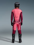 Motocrossrijder van de achterkant in Alpinestars 2026 Racer Riway-broek in Dark Red Coral, bijpassende jersey, zwarte helm, handschoenen en laarzen, met een opvallend 'astars'-logo op het zitvlak en een tweekleurig rood ontwerp.