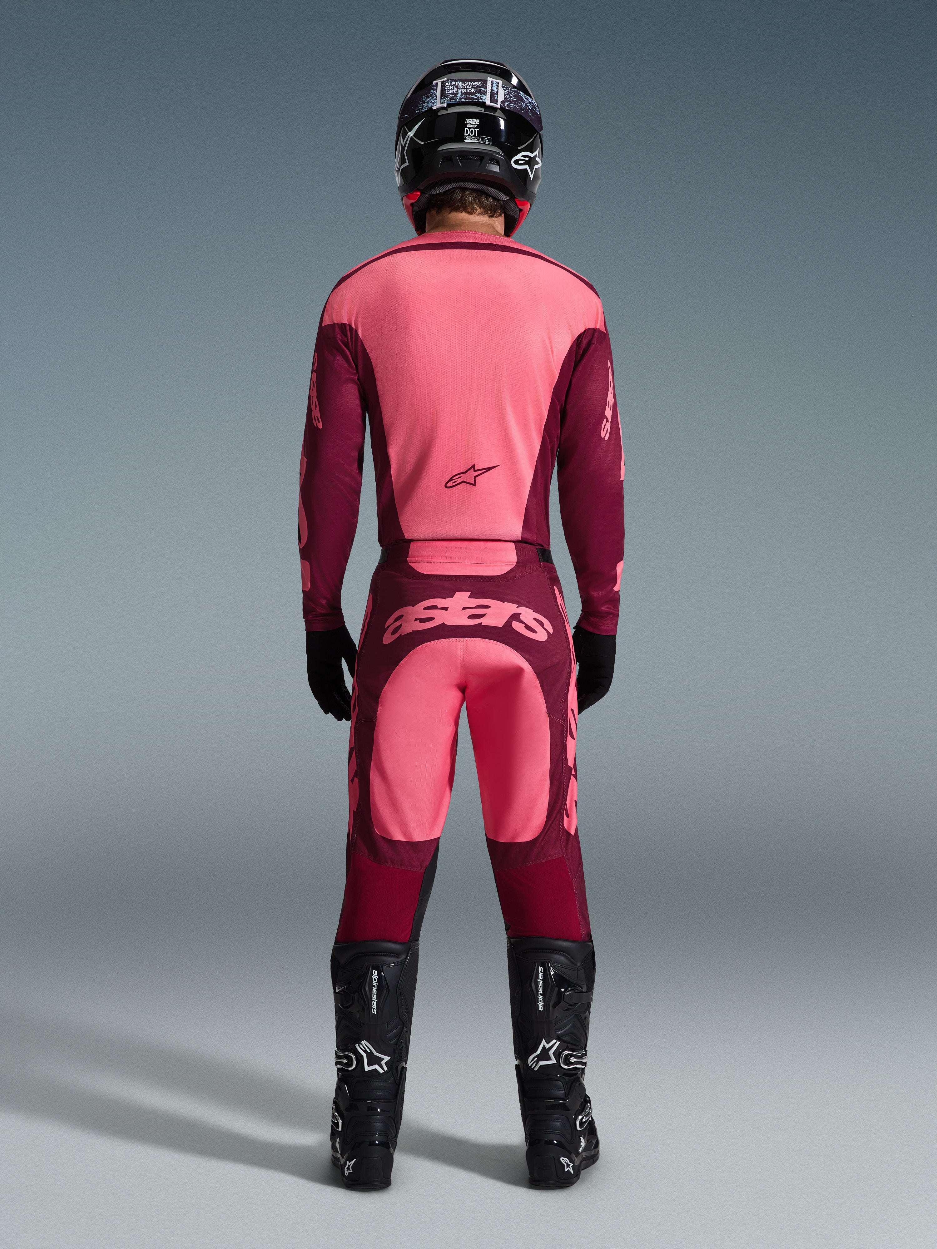 Motocrossrijder van achteren gezien in het Alpinestars 2026 Racer Riway Jersey en bijpassende broek in Dark Red Coral, met zwarte laarzen, een zwarte helm en zwarte handschoenen, gecoördineerde high-performance uitrusting voor off-road racen