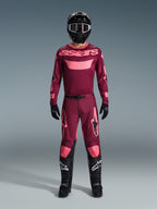 Motocrossrijder in volledige race-uitrusting, 2026 Racer Riway Jersey in Dark Red Coral, bijpassende donkerrode broek met koraalrode accenten, zwarte helm met witte accenten, zwarte laarzen met witte logo's en zwarte handschoenen, gecoördineerde outfit voor off-road racen