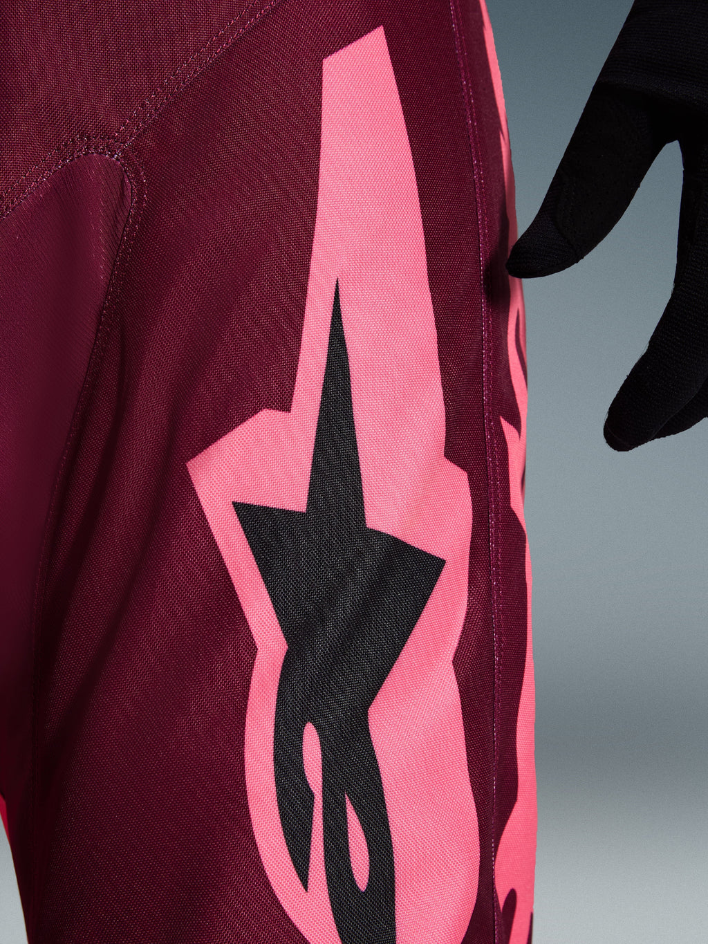 Alpinestars 2026 Racer Riway broek, motorcross broek, Dark Red Coral, detailopname van een grote hoekige koraalroze graphic en zwart sterlogo, met focus op de duurzame polyfabric textuur en prestatiegerichte stiksels.