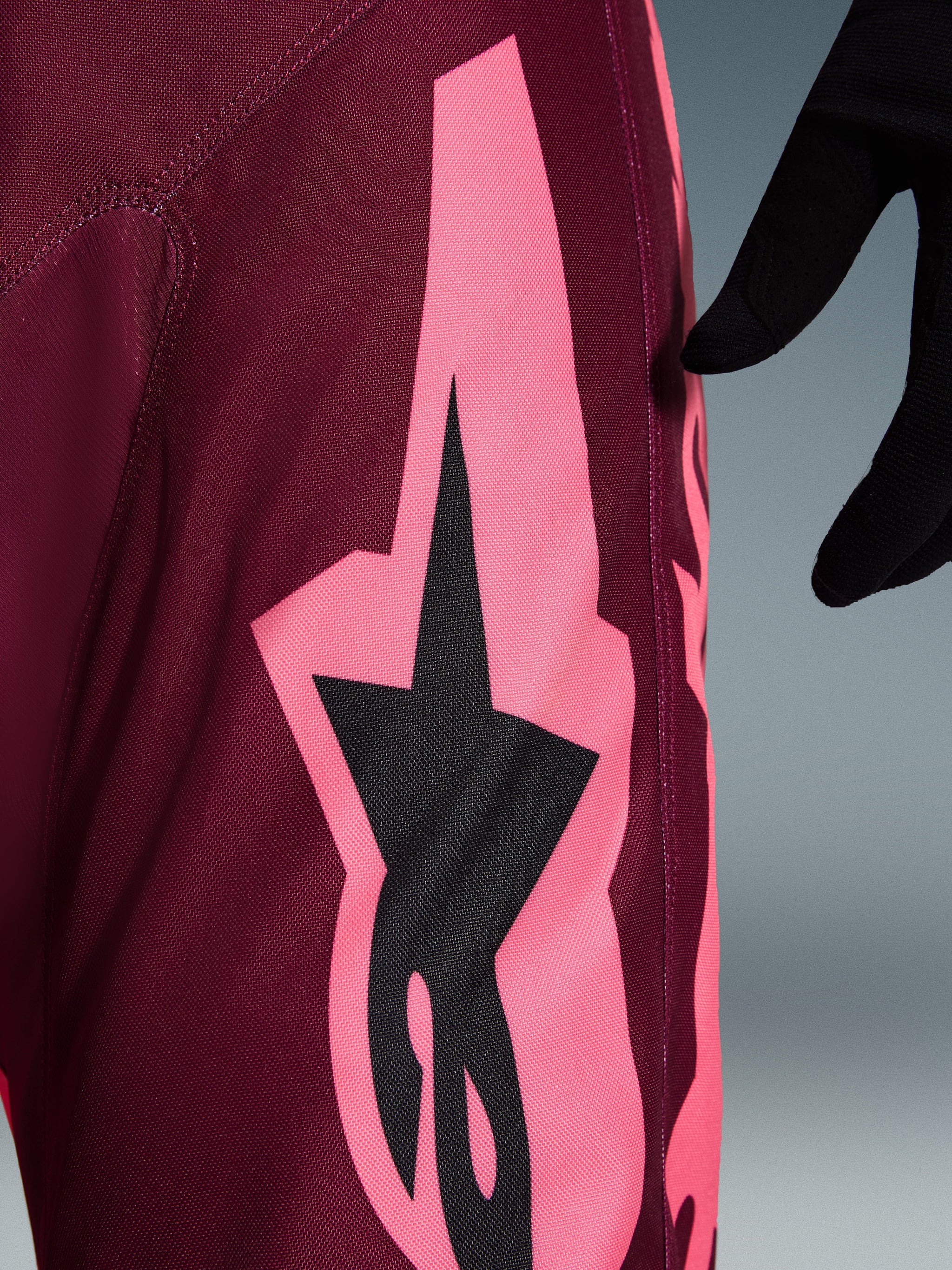 Alpinestars 2026 Racer Riway broek, motorcross broek, Dark Red Coral, detailopname van een grote hoekige koraalroze graphic en zwart sterlogo, met focus op de duurzame polyfabric textuur en prestatiegerichte stiksels.