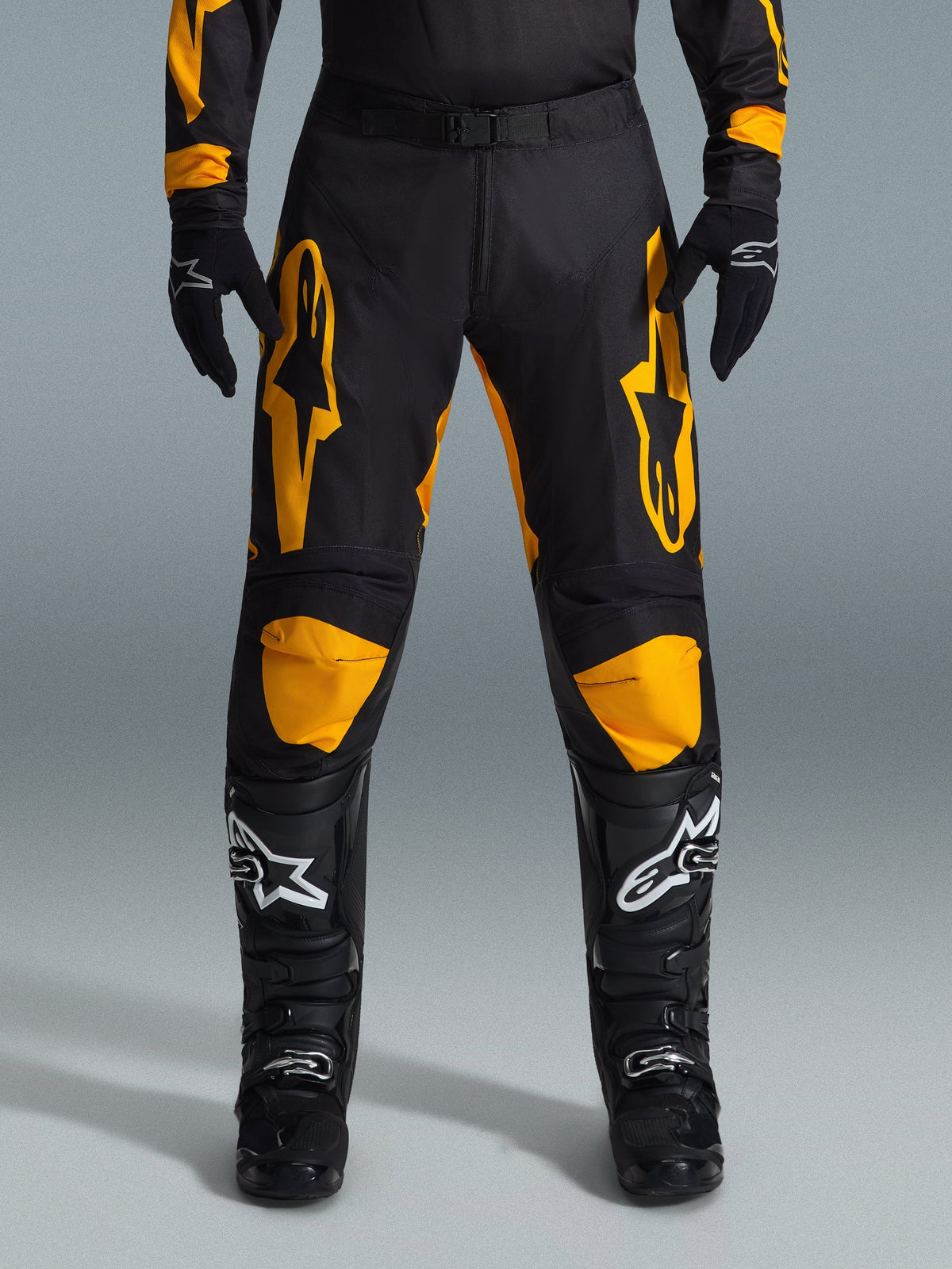 Alpinestars 2026 Racer Riway Pants, motocross broek, geel en zwart, gedragen met zwarte motocross handschoenen en zwarte laarzen met witte logo's, voorzien van grote gele Alpinestars logo's op de dijen en gele kniepanelen, duurzaam ontwerp voor off-road raceprestaties
