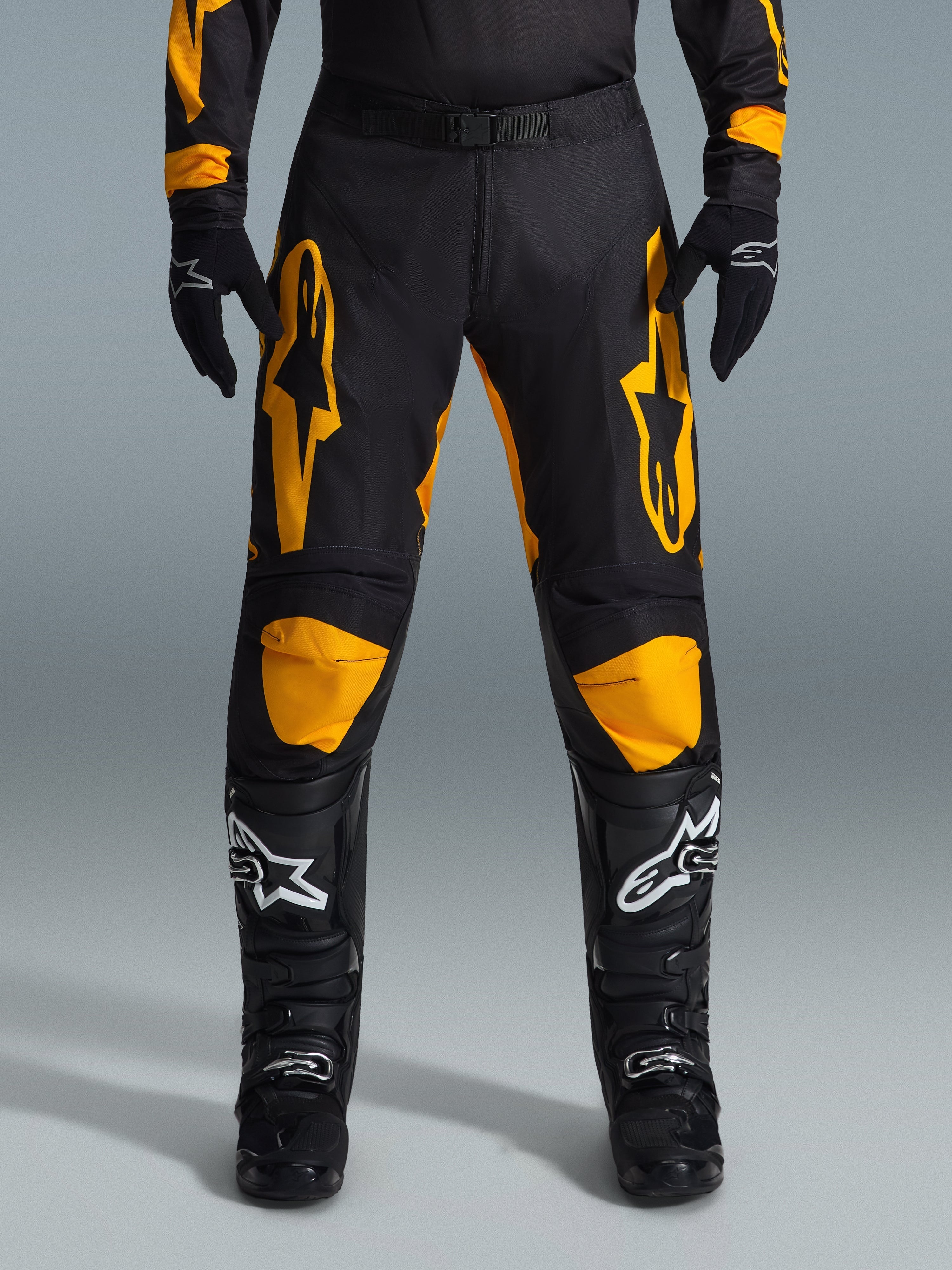 Alpinestars 2026 Racer Riway Pants, motocross broek, geel en zwart, gedragen met zwarte motocross handschoenen en zwarte laarzen met witte logo's, voorzien van grote gele Alpinestars logo's op de dijen en gele kniepanelen, duurzaam ontwerp voor off-road raceprestaties