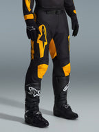 Alpinestars 2026 Racer Riway broek, motorcrossbroek, geel en zwart, gedragen met zwarte handschoenen en zwarte motorcrosslaarzen, met opvallende gele Alpinestars-branding en knie-accenten op een zwarte basis, ontworpen voor hoogwaardige off-road prestaties.