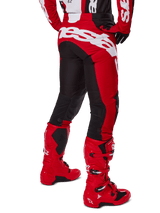Alpinestars 2025 Racer Veil broek, motorcross broek, zwart en felrood, achteraanzicht met groot wit Alpinestars-logo op het zitvlak, zwarte stretchpanelen op de achterkant van de benen, gedragen met bijpassende rode racelaarzen, duurzame off-road race-uitrusting